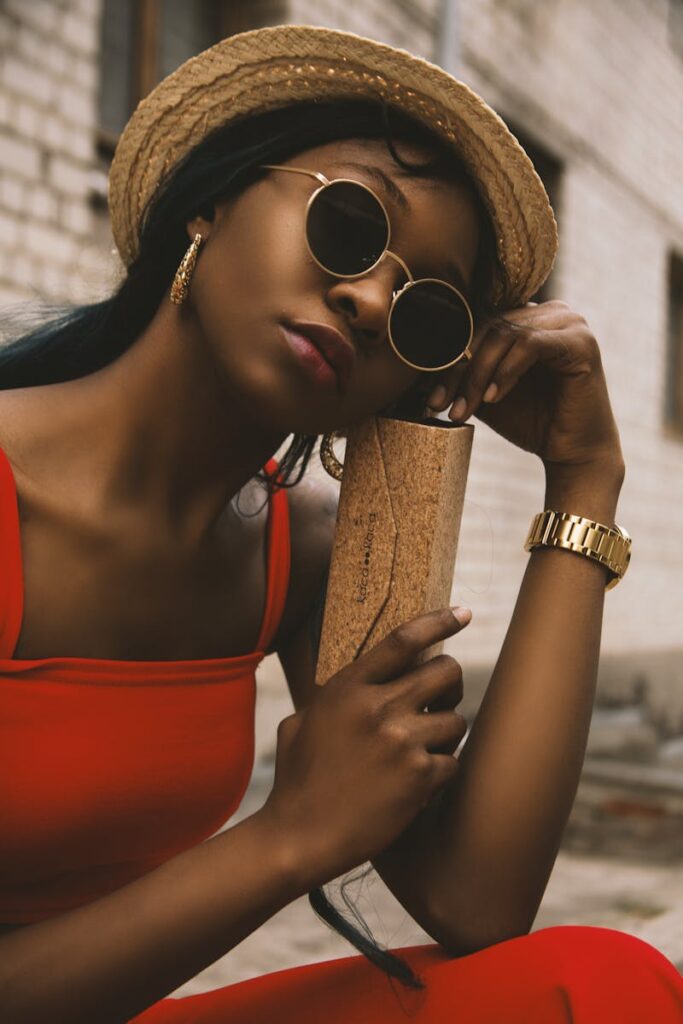 Chic portrait of a fashionable woman in outdoors setting, wearing sunglasses and a straw hat.