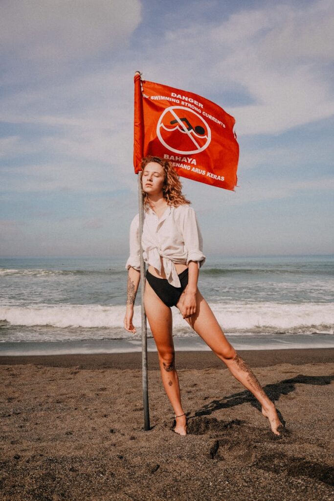 Woman leaning on danger sign pole on beach with sea in background