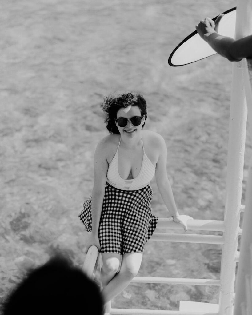 A fashionable woman with sunglasses poses on a railing during a sunny day.