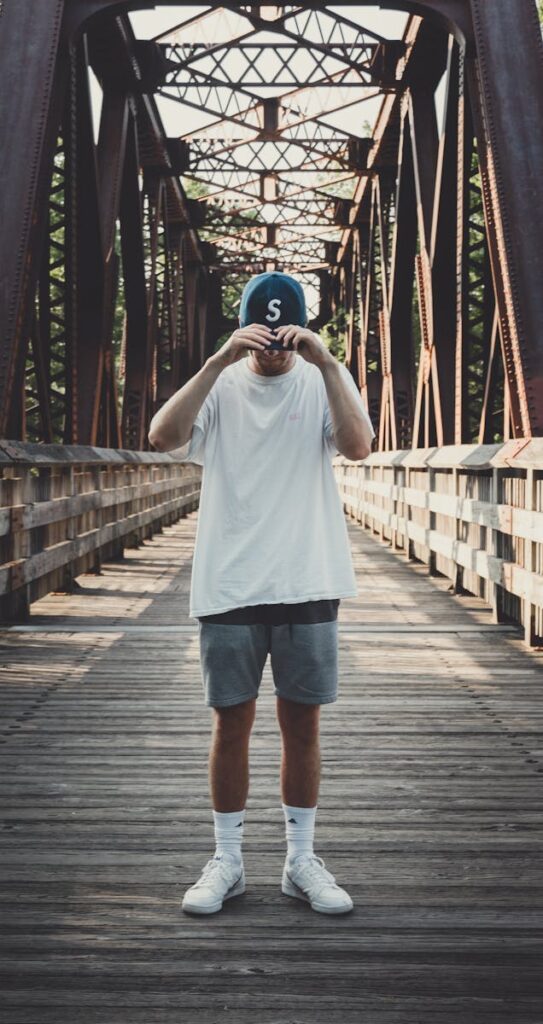 Casual fashion photo of a man posing on a metal bridge on a sunny day.