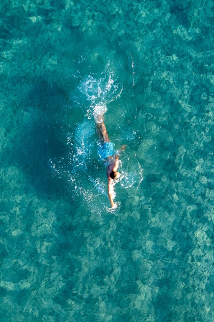 Top-down drone shot of a man swimming in clear turquoise waters in Alaçatı, Turkey.