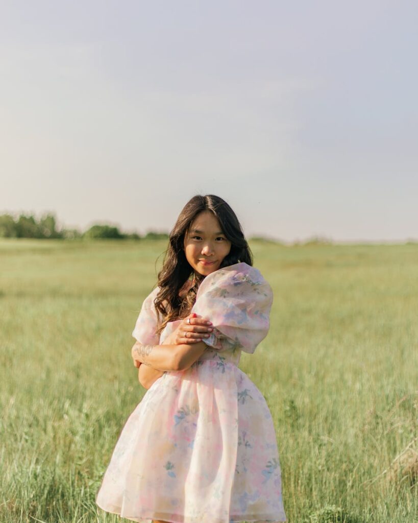 A young woman in a floral pastel dress standing in a sunlit meadow, exuding a serene and joyful vibe.