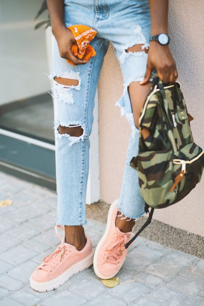 Fashionable young woman in ripped jeans and pink sneakers outdoors.