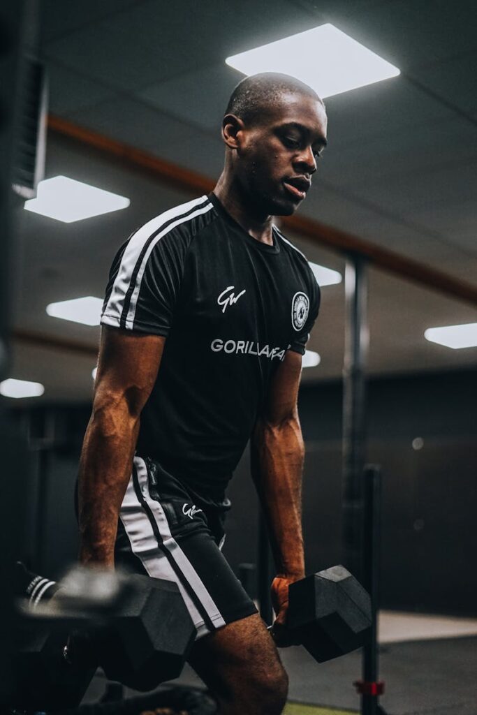 African American man lifting dumbbells in a gym, showcasing focus and strength during a workout session.