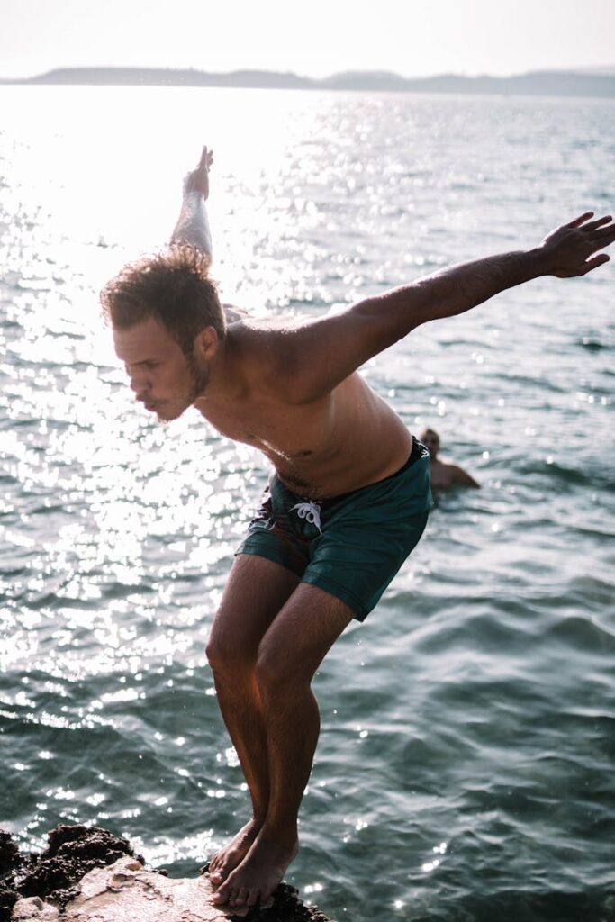 A young man prepares to dive into the sparkling ocean on a sunny day, enjoying outdoor fun.