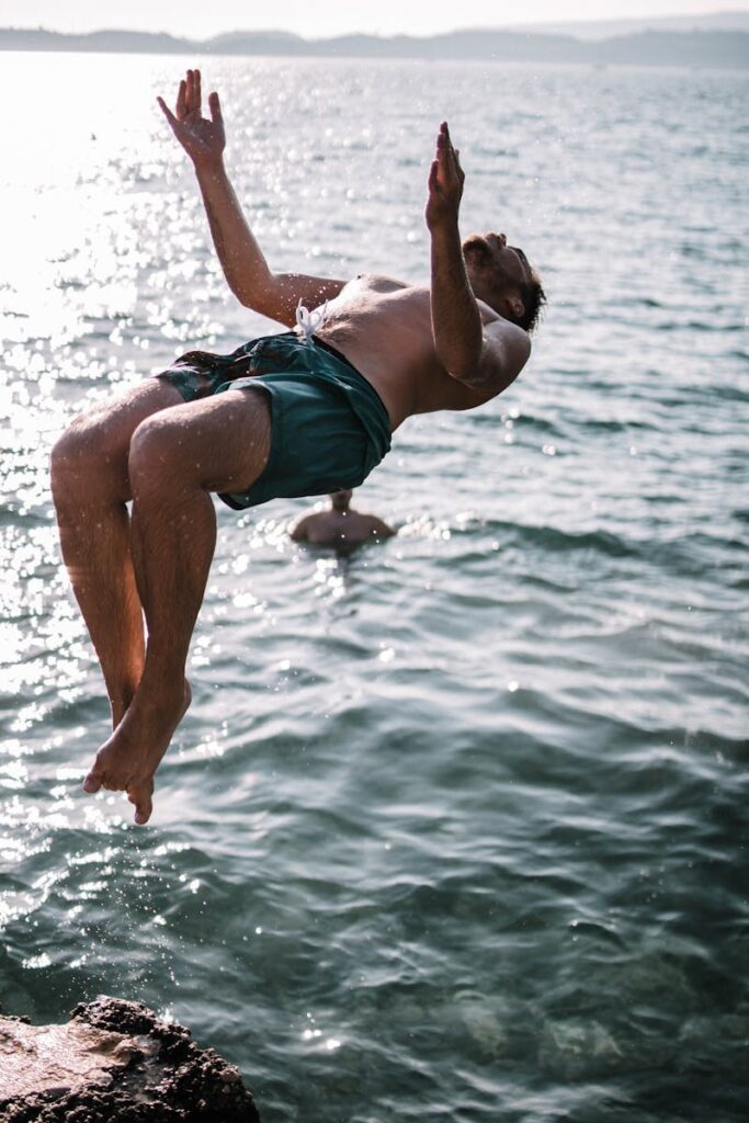 A young man enjoying a summer day by performing a backflip into the ocean.