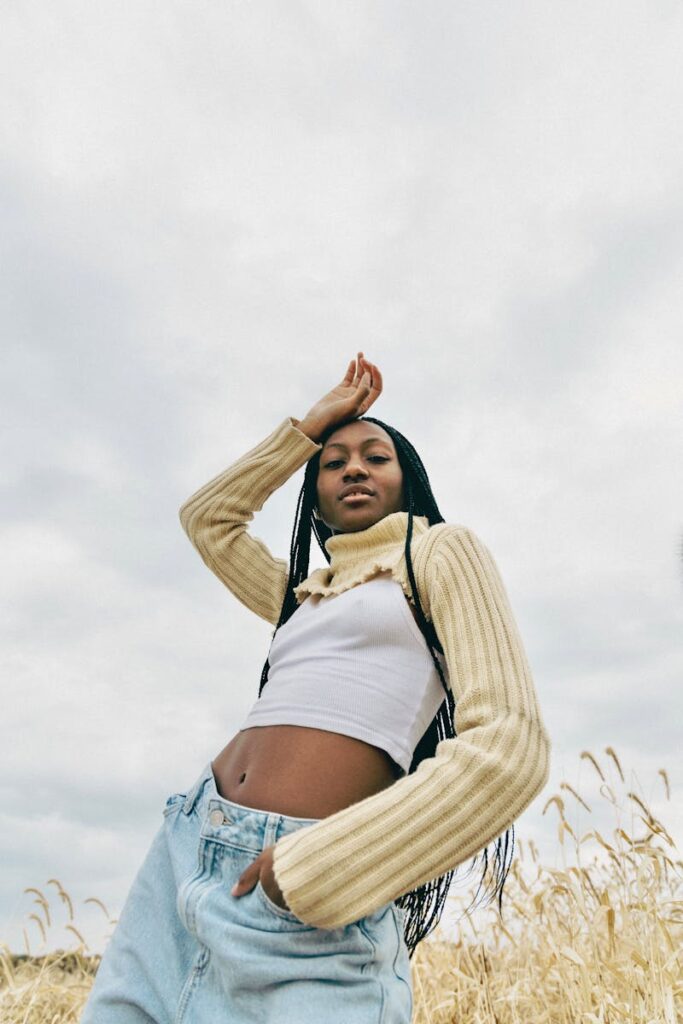 Stylishly dressed woman poses confidently in a Montreal field against a cloudy sky.