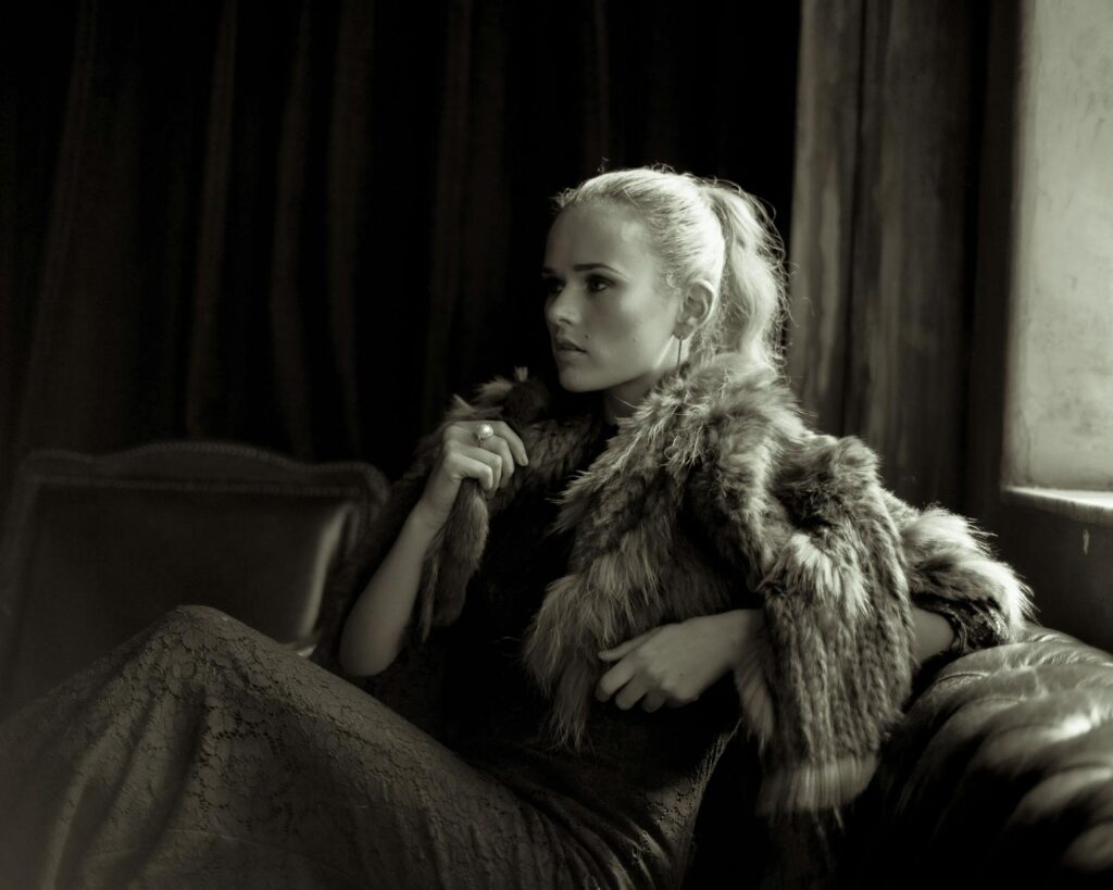 Sophisticated woman wearing fur coat, posing elegantly in luxurious interior.