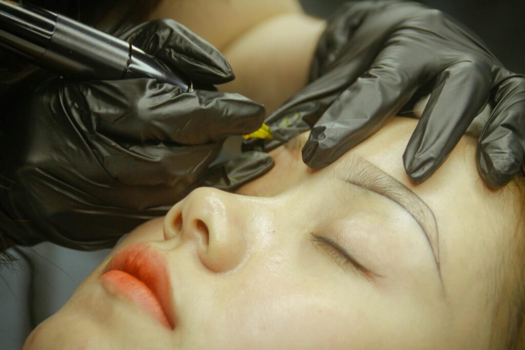 A detailed view of eyebrow microblading procedure with gloved hands and closed eyes.