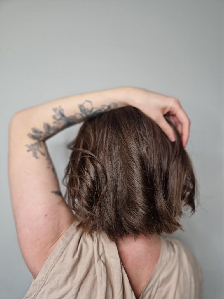 Elegant portrait showcasing a woman with tattoos and a trendy bob haircut against a gray background.