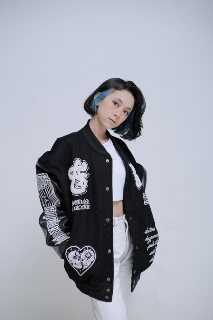Young woman in a letterman jacket posing with style in a studio setting.