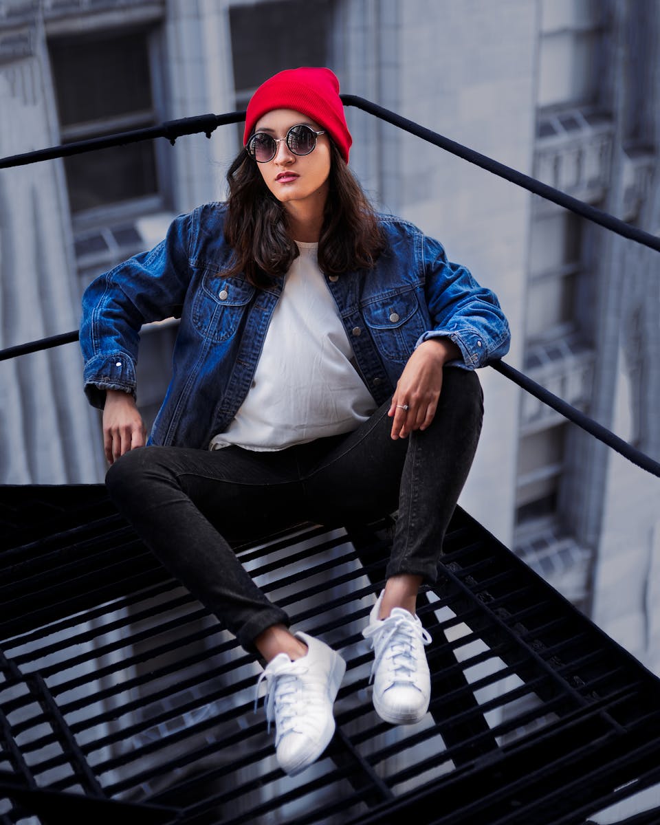 Stylish woman in a red beanie poses on a fire escape in an urban environment.