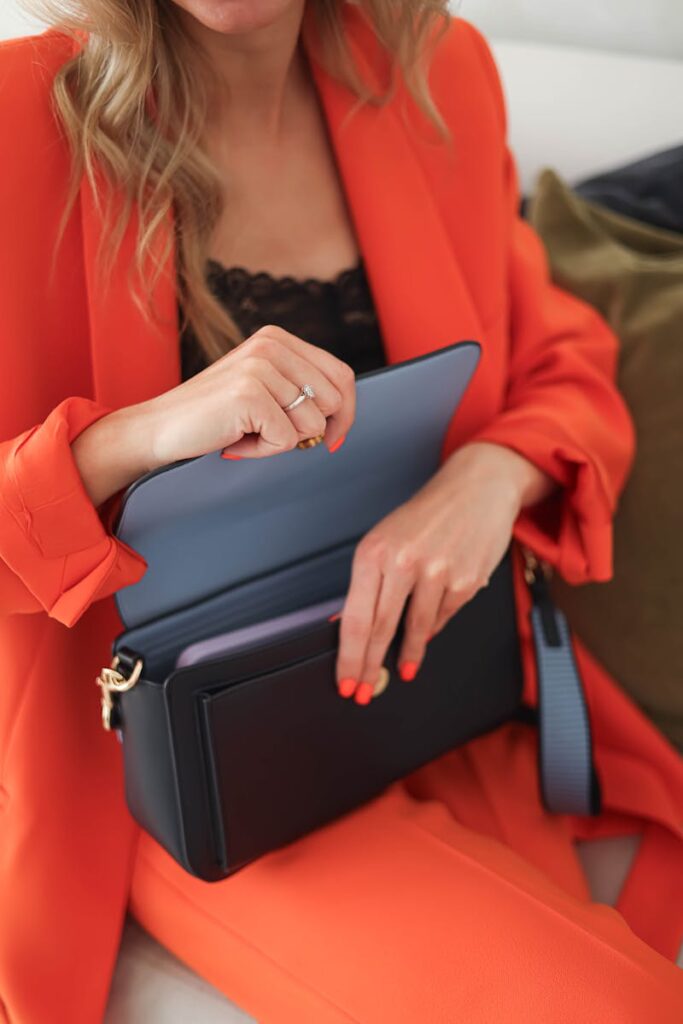 Woman in bright suit holding an elegant leather clutch bag, emphasizing fashion and style.