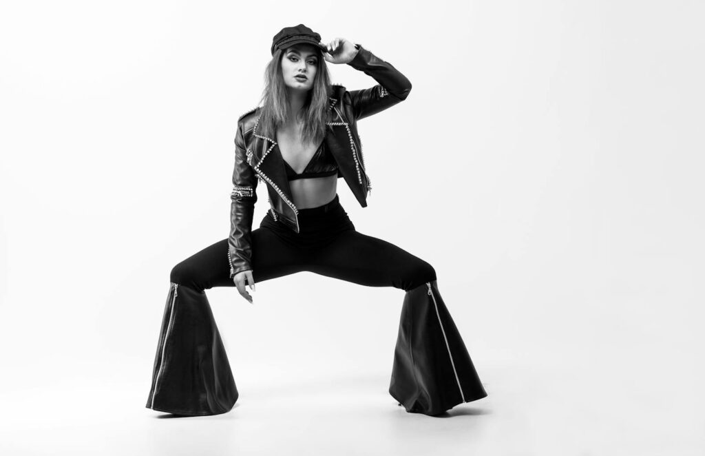 Stylish fashion model posing in a black and white studio shoot, wearing bell bottoms and a leather jacket.