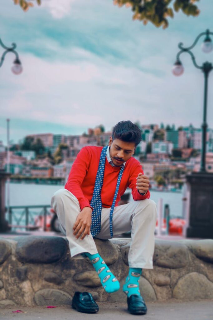 Stylish man in bright attire sitting by a scenic riverfront area, exuding a modern fashion sense.