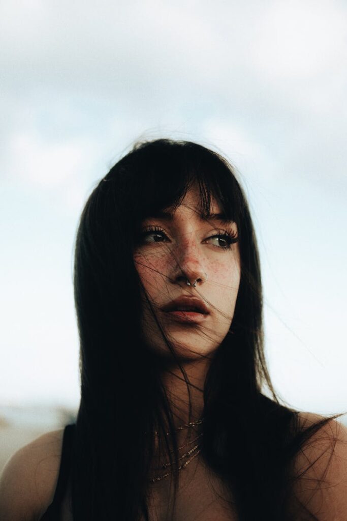 A young woman with bangs gazes into the distance against a clear sky.