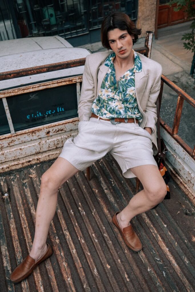 A stylish man in a floral shirt and linen suit relaxes in a pick-up truck outdoors.