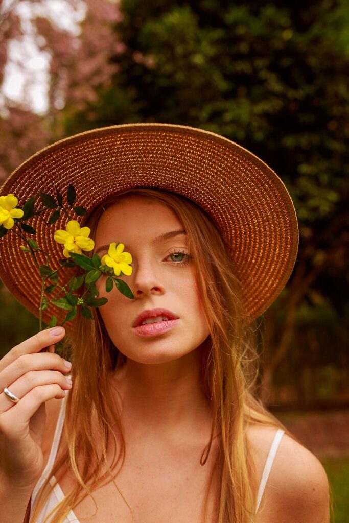 A woman wearing a straw hat holding yellow flowers in a serene outdoor setting.