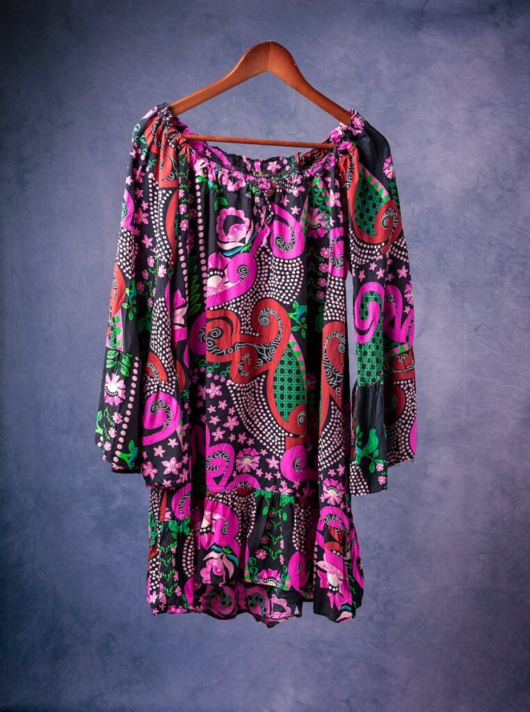 Colorful tunic dress with swirls and floral abstract patterns on a hanger.