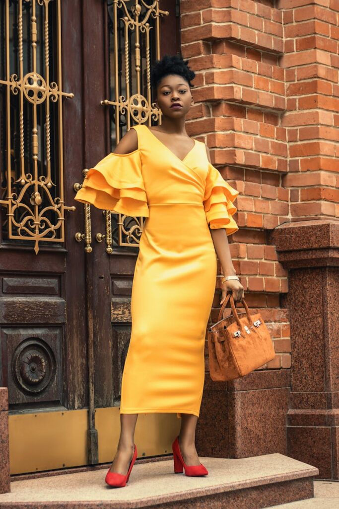 Fashionable woman in a yellow dress poses elegantly against a classic brick backdrop.