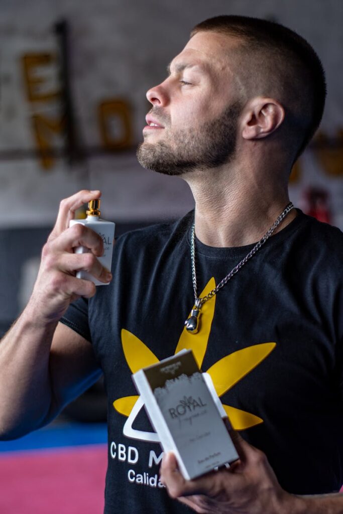 A bearded man applies perfume, displaying masculinity and confidence indoors.