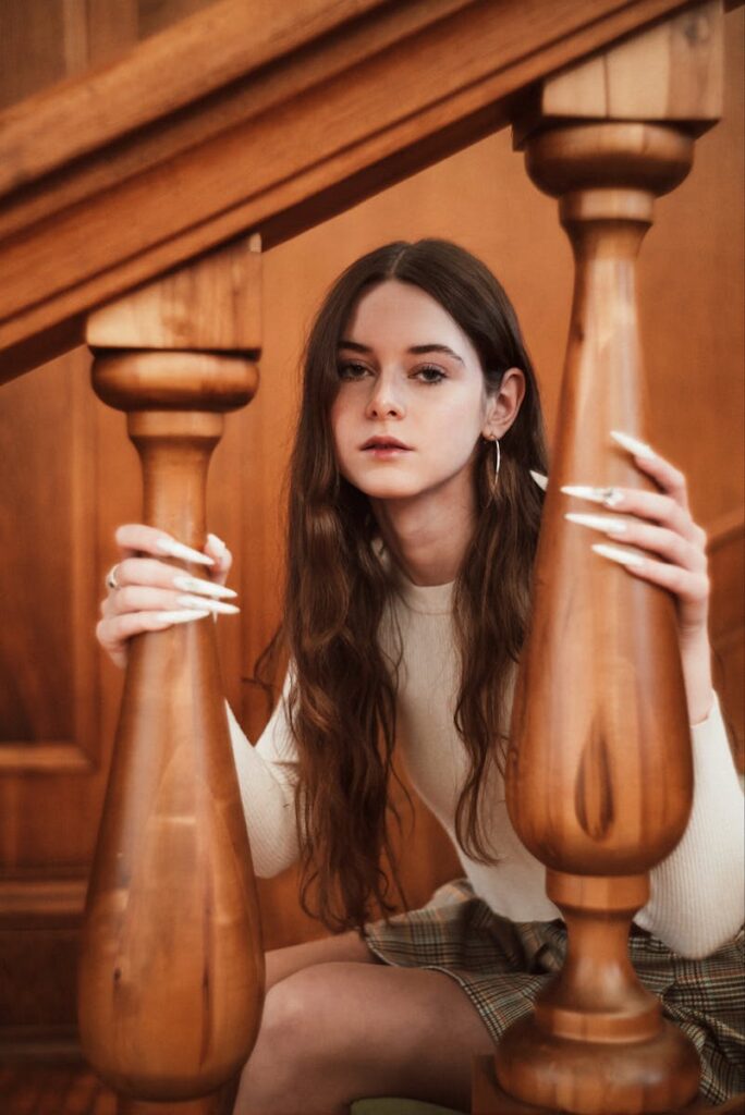 Elegant young woman posing with striking nails and a skirt beside a wooden railing.