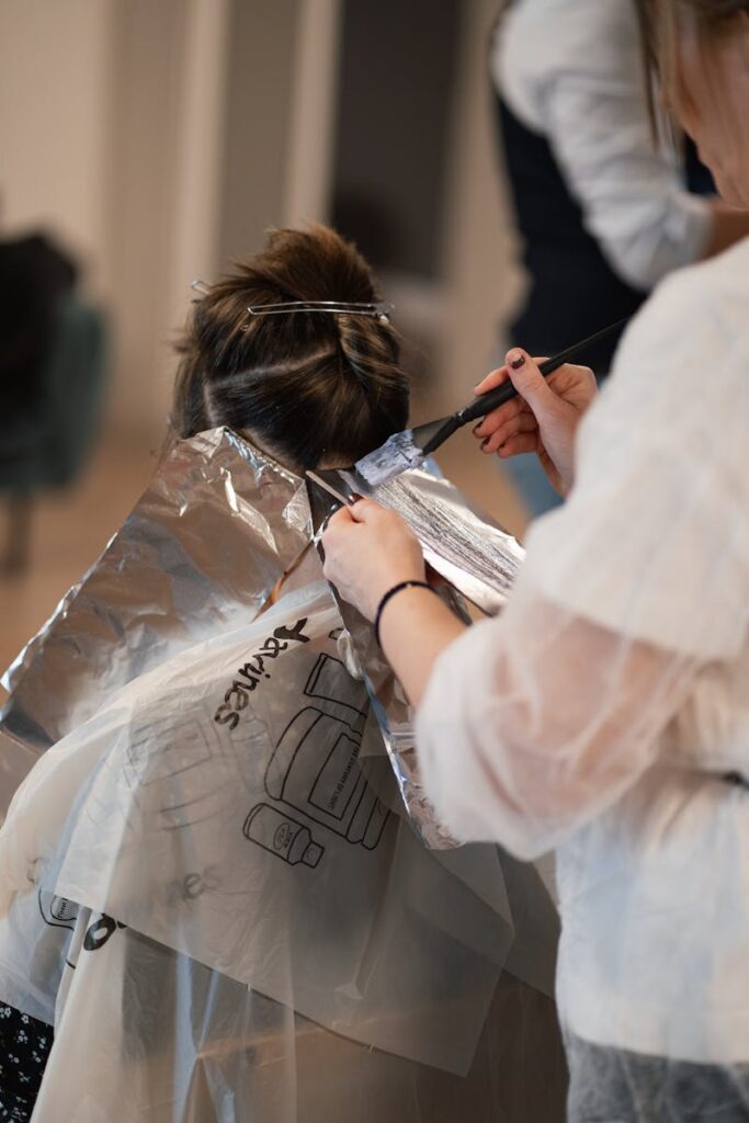 A stylist applies hair color to a client in a professional salon setting.