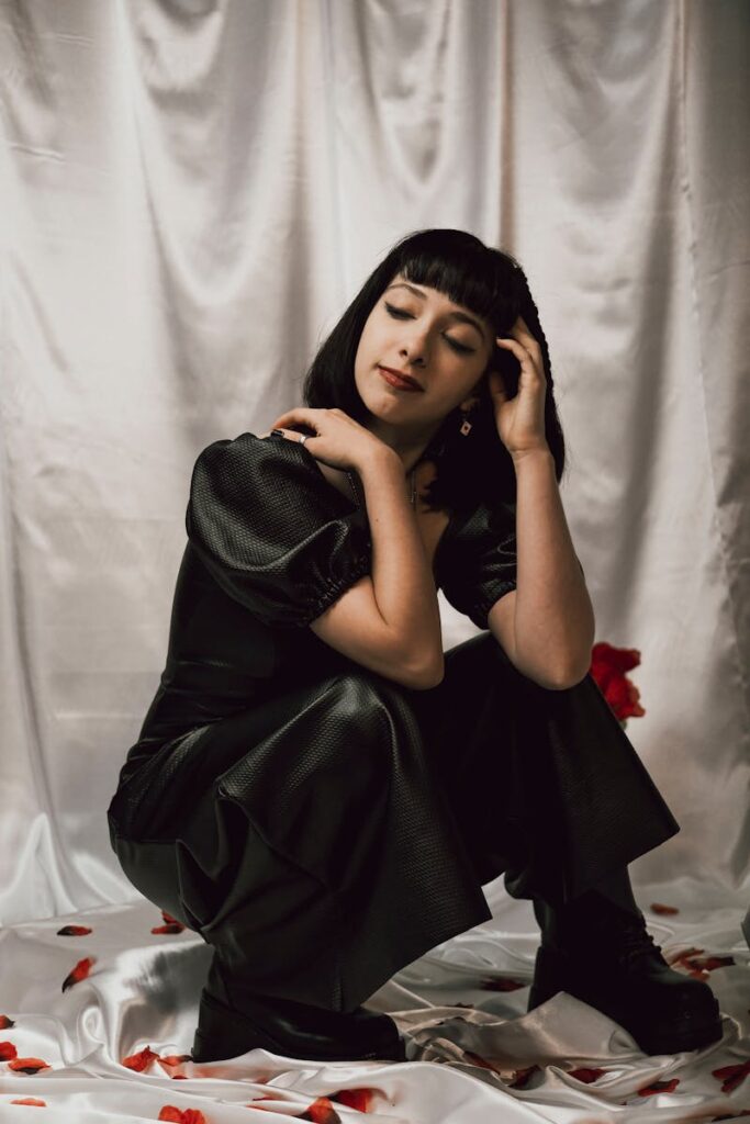 Stylish gothic woman in black with roses, sitting indoors, exuding elegance.