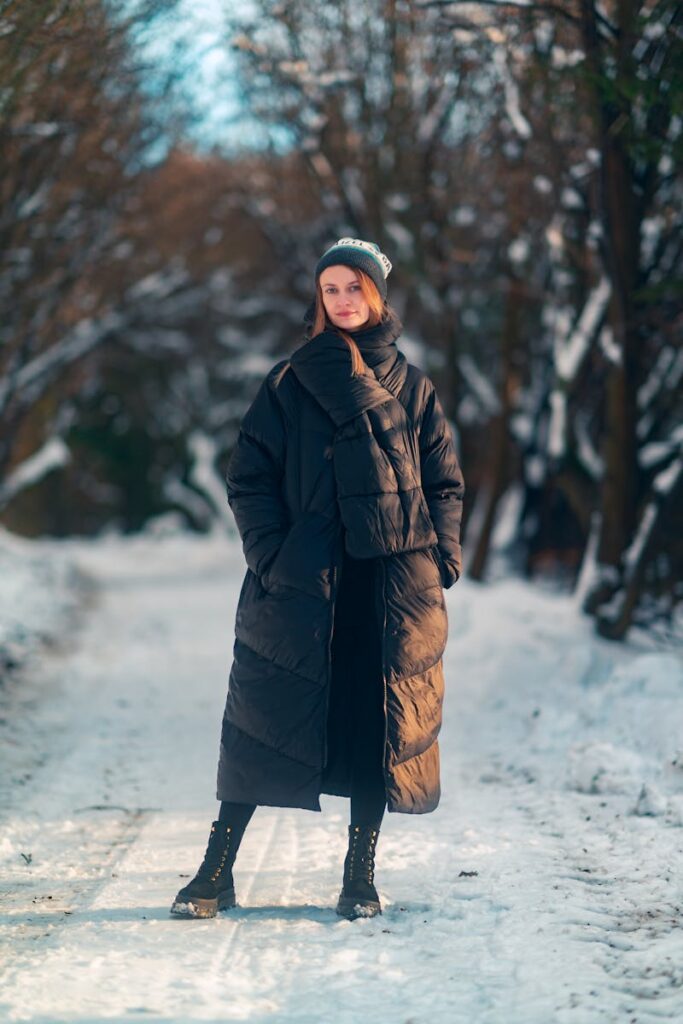 Stylish woman in a puffer coat standing on a snowy path in a forest.