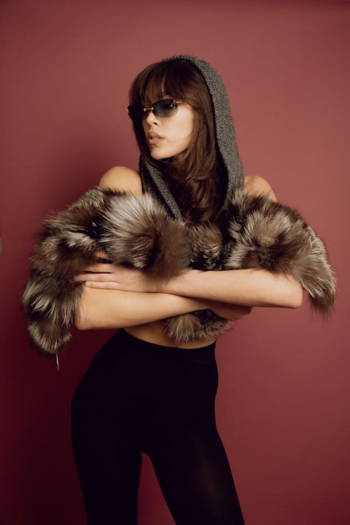 Fashionable woman posing with fur stole and sunglasses against a red background in a studio.