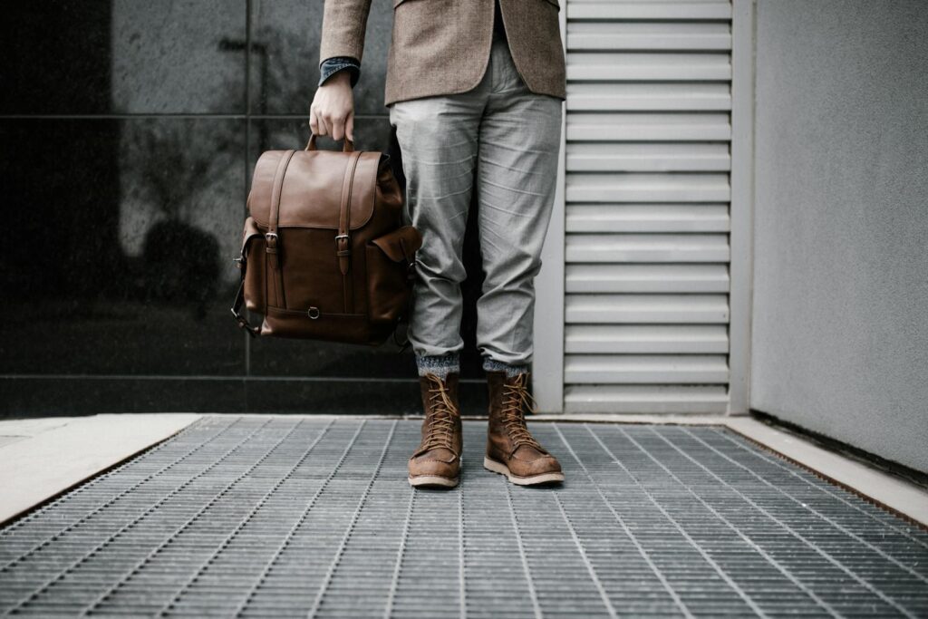 A man in stylish attire holding a leather backpack outdoors.