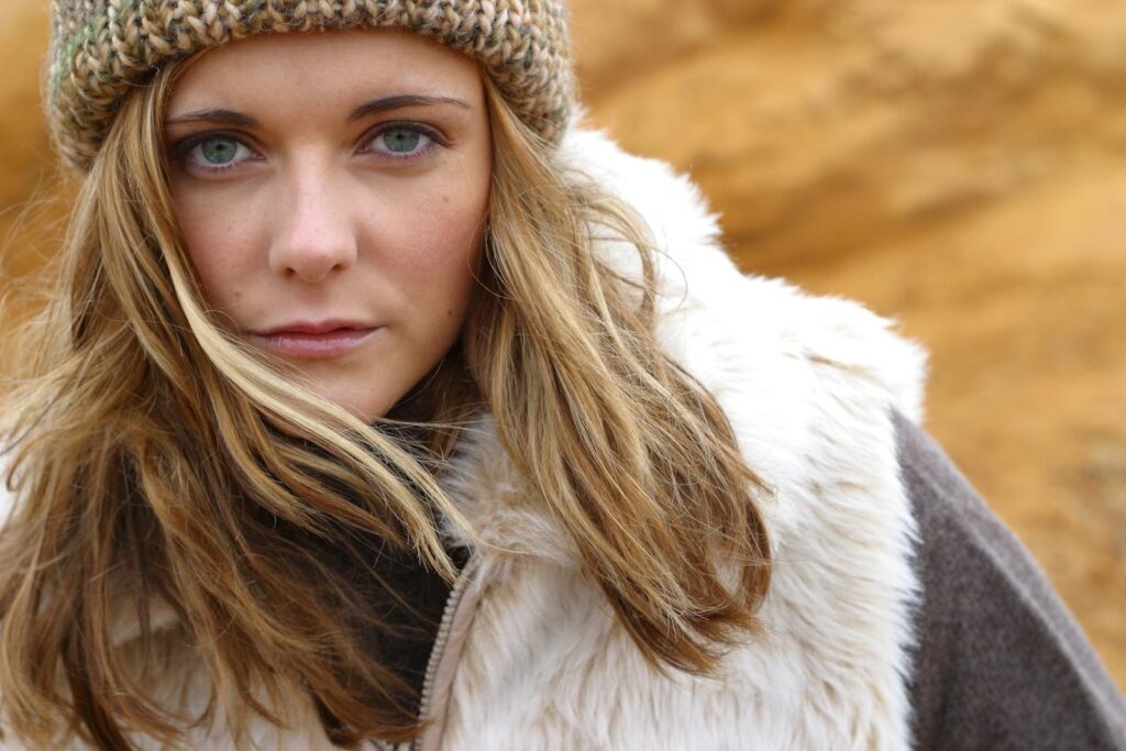 Close-up portrait of a woman in a beanie and fur coat outdoors, exuding a winter vibe.