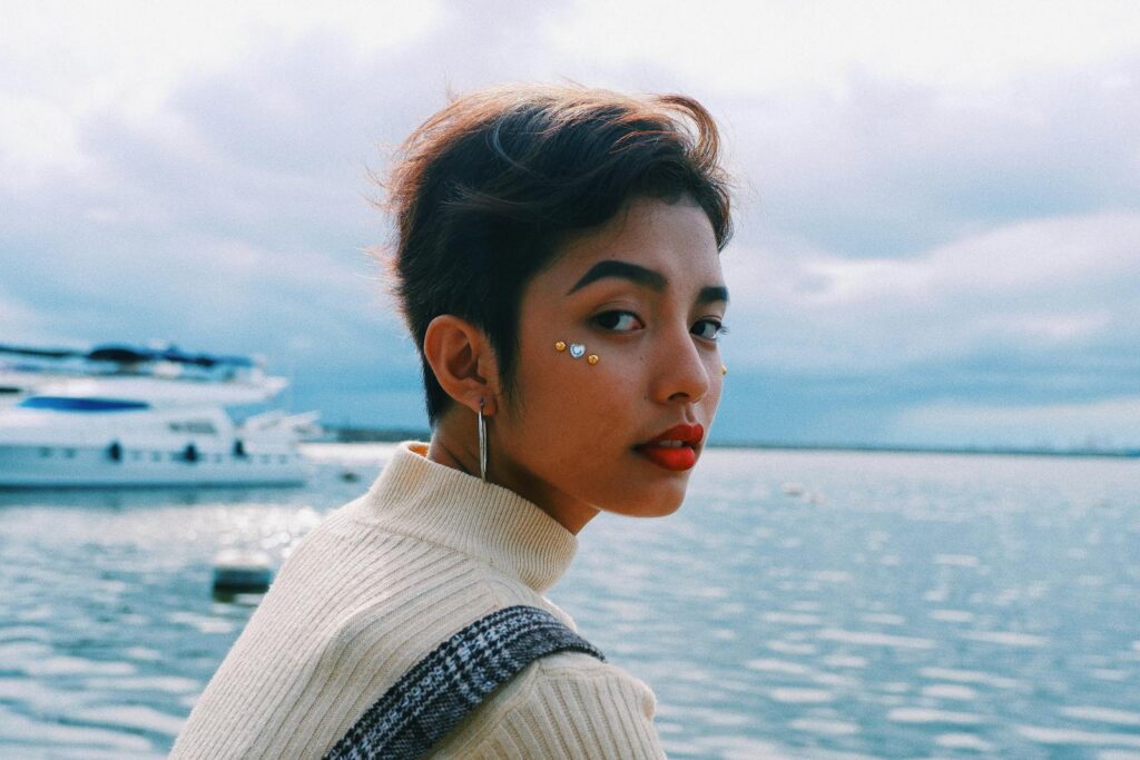 A stylish young woman with vibrant red lips poses gracefully by the seaside.