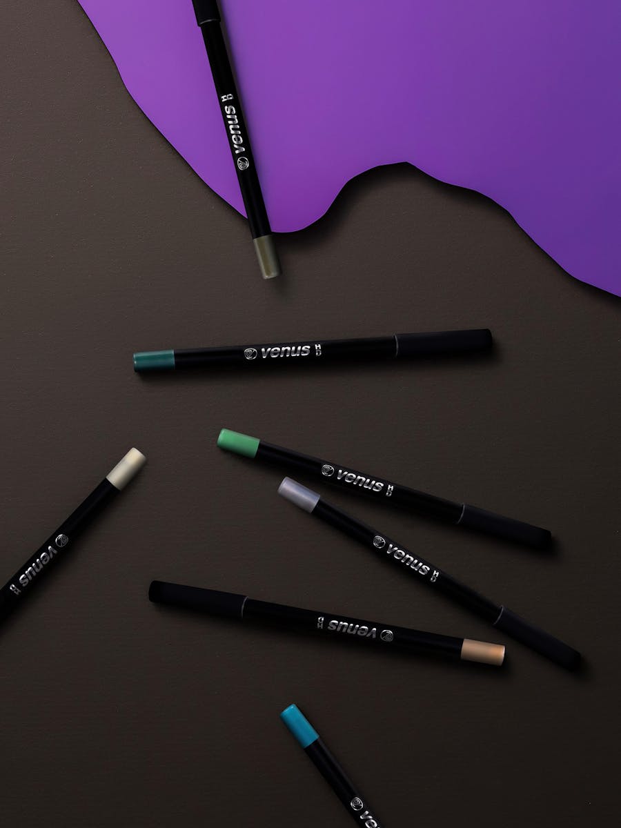 Stylish arrangement of vibrant eyeliners on a rich dark backdrop with purple accents, perfect for beauty and fashion editorial.