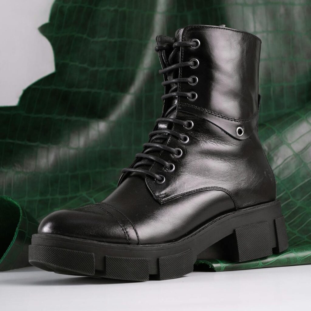 High angle view of a shiny black leather combat boot with green background.