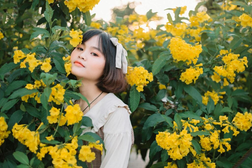 Asian woman amidst vibrant yellow flowers in an outdoor portrait.