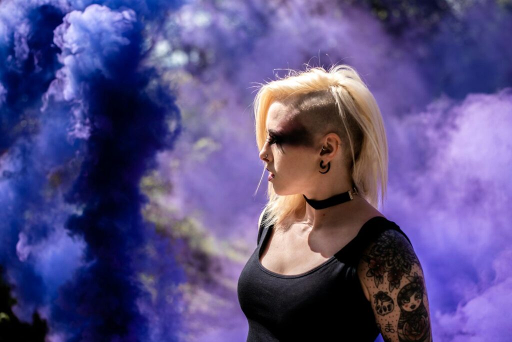 Artistic portrait of a woman with smoke, showcasing dramatic purple hues and edgy fashion.
