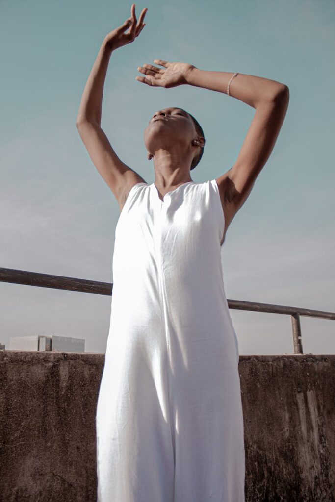 A serene woman stands on a rooftop with arms uplifted, embracing tranquility.