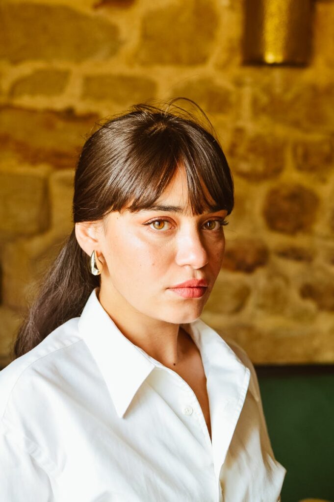 Portrait of a woman in a white shirt against a stone wall background.