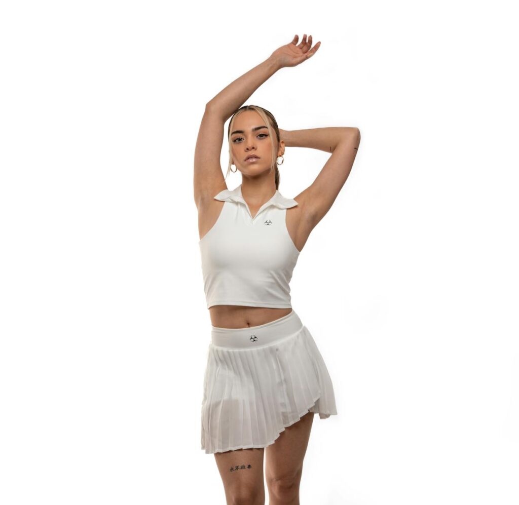 Woman posing in stylish white tennis outfit against a white background, embodying modern sports fashion.