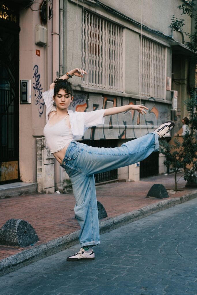 Casually dressed ballet dancer strikes a pose on a city street with graffiti background.