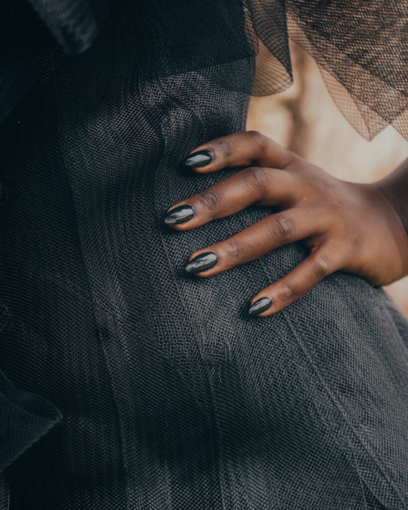 Elegant hand with black nail polish resting on textured fabric, invoking sophistication.