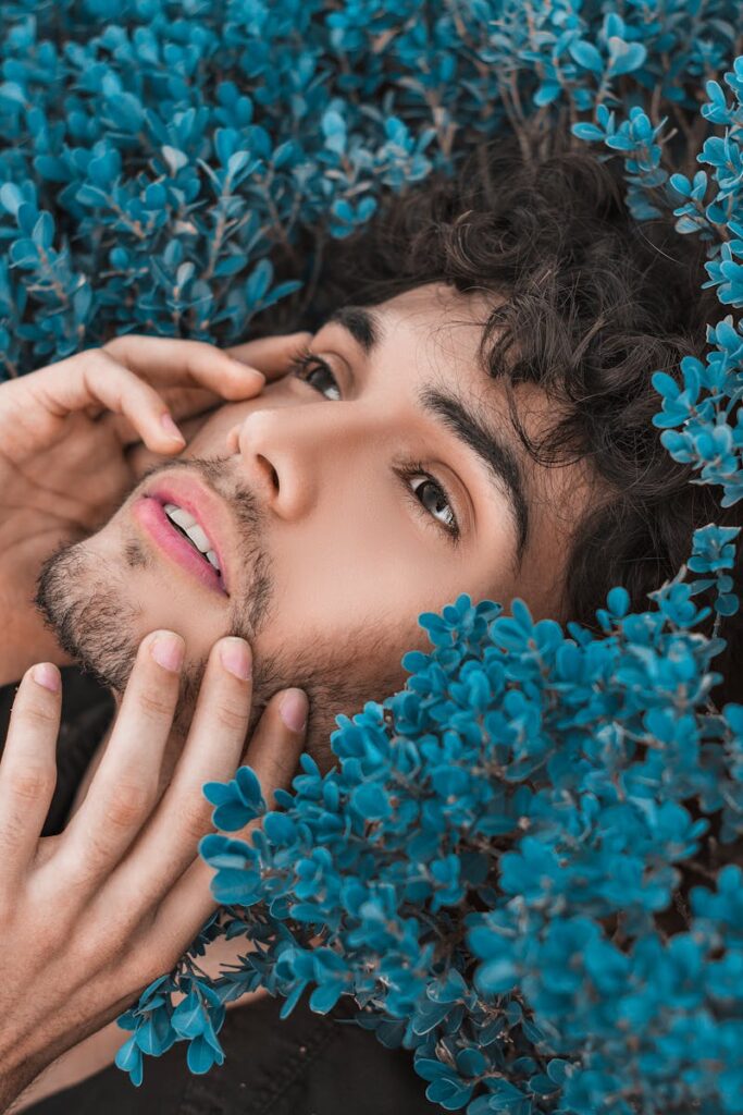 Close-up portrait of a man surrounded by vibrant blue flowers, expressing a serene mood.