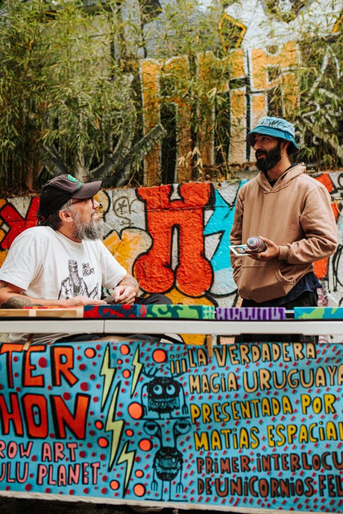 Street artists conversing near colorful graffiti in an outdoor setting.