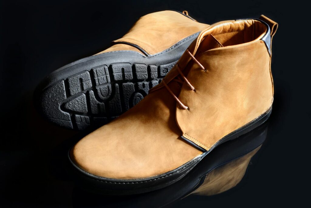 Pair of fashionable leather boots with textured soles on a reflective surface.