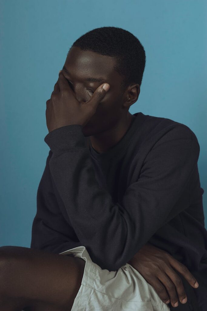 Young man in deep thought posed against a blue backdrop, captured softly.