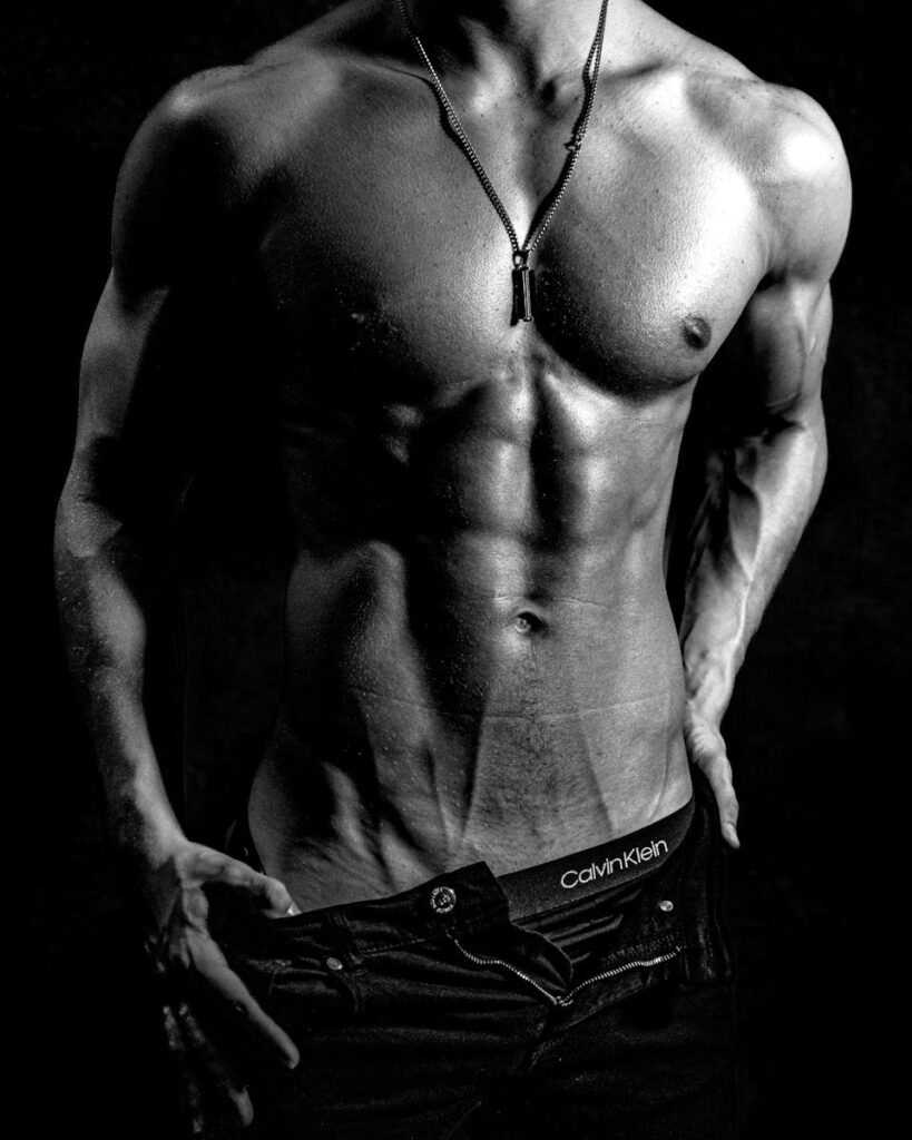 Striking black and white image of a shirtless muscular male model posing confidently.