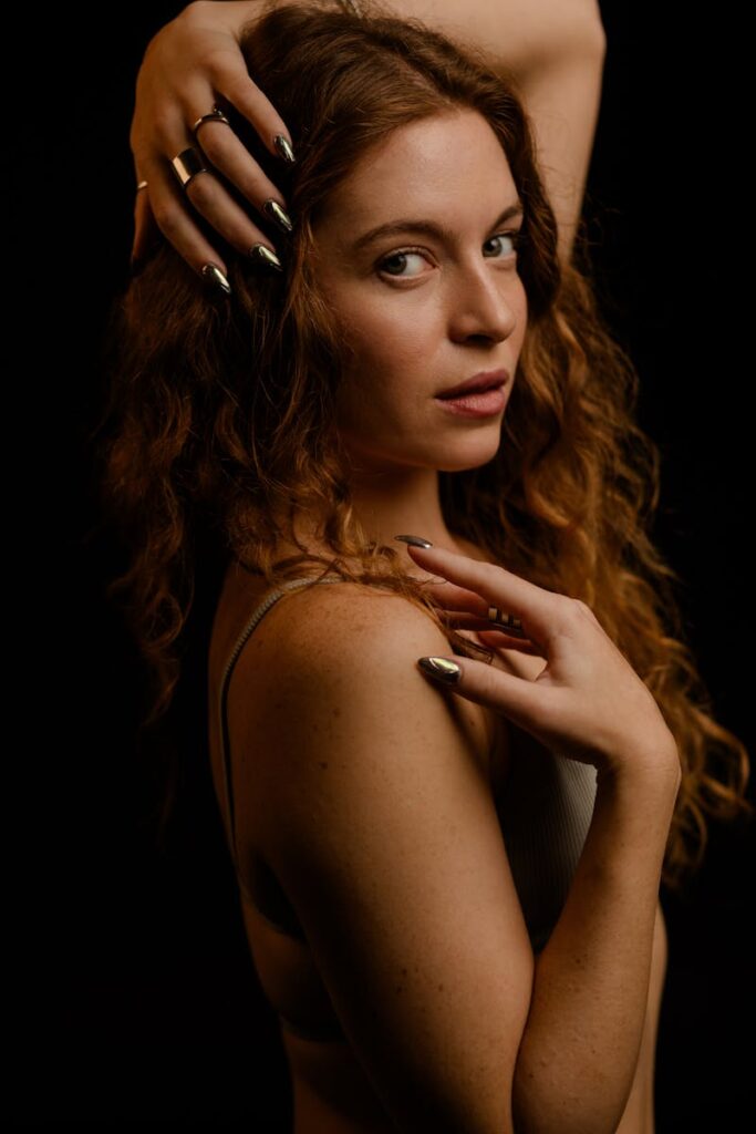 A captivating portrait of a woman with curly hair and metallic nails posing gracefully.