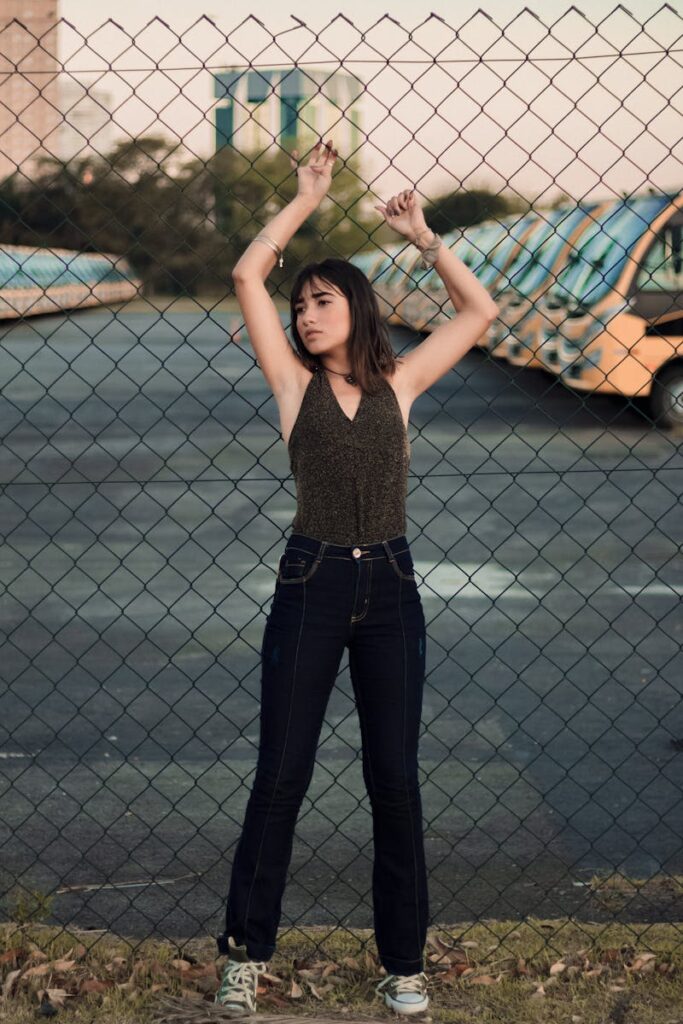 Fashion portrait of a woman posing against a chain-link fence in an urban setting.