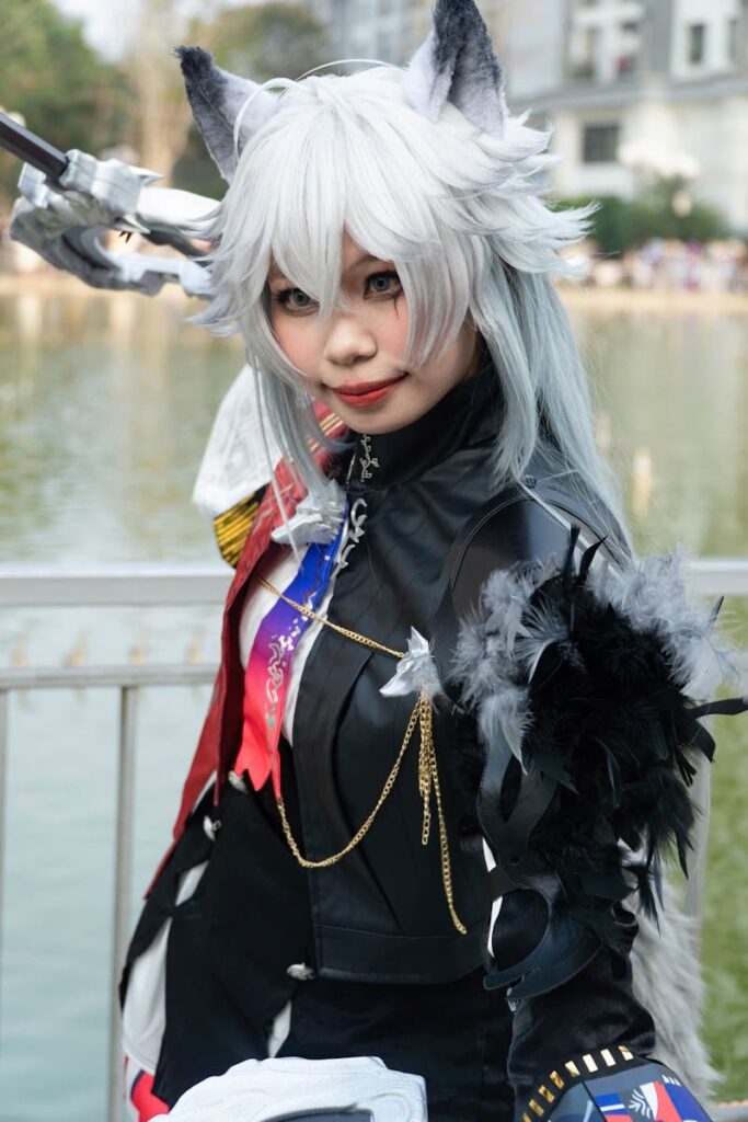A cosplayer dressed as a character with wolf ears poses by a lake.